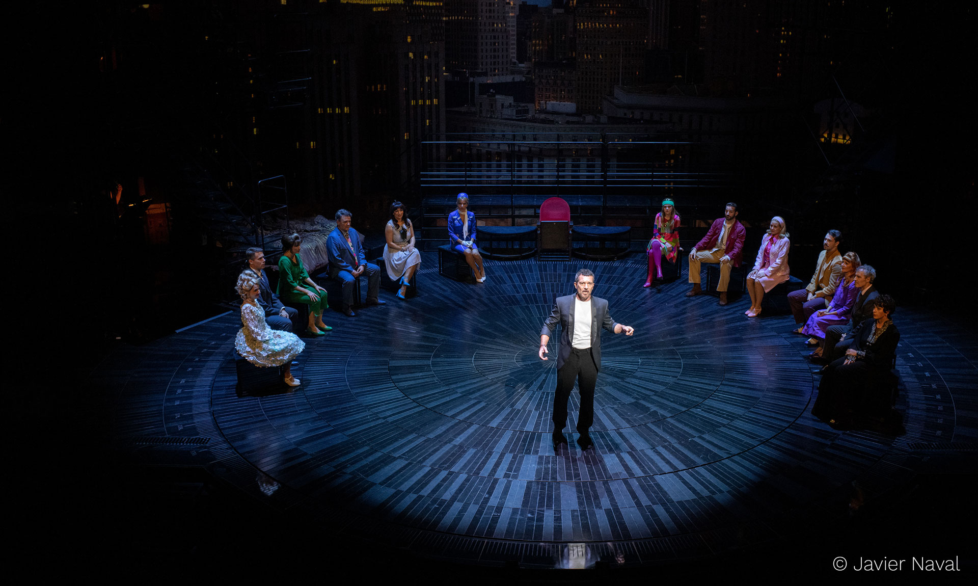 Ein Mann im Frack steht singend auf einer beleuchteten Bühne mit sitzendem Publikum